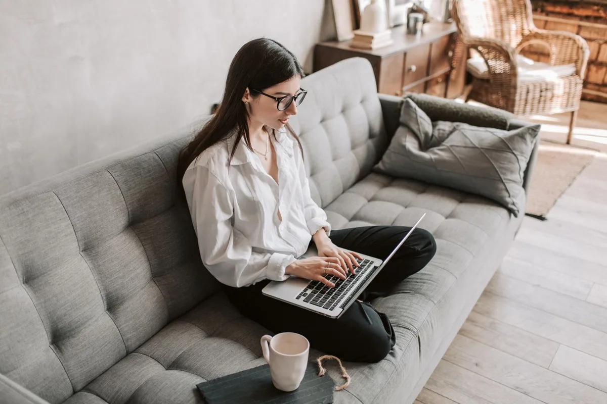 A woman reviewing work on a laptop with a notebook beside her.