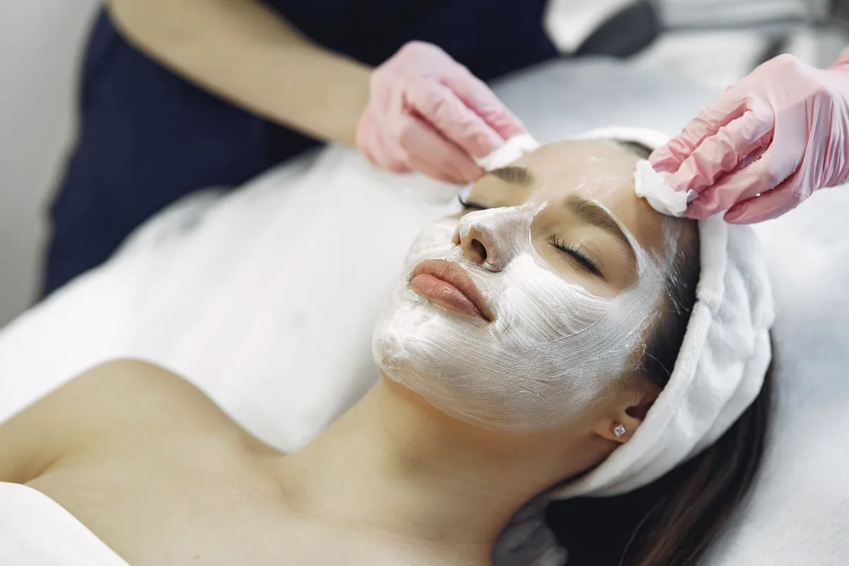 A salon practitioner applying a facial mask with a brush.