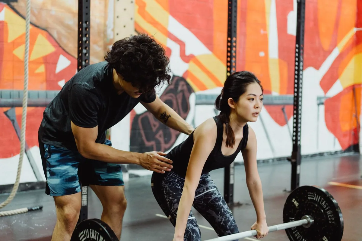 A trainer coaching a woman lifting a barbell in a gym.