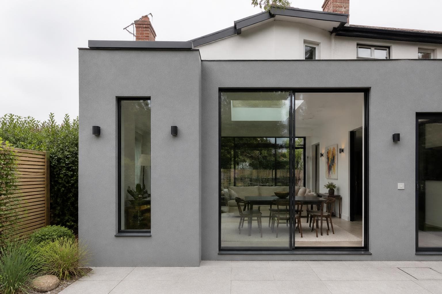 Slim black aluminium windows and sliding doors on a modern grey rendered UK house extension.