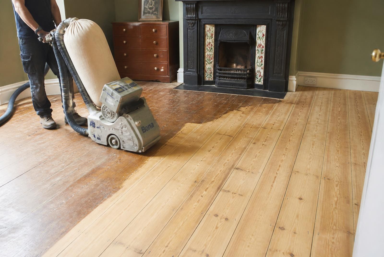 Contractor sanding an old Victorian pine floorboard floor with a dust extracted drum sander, half the floor sanded back to bare timber.