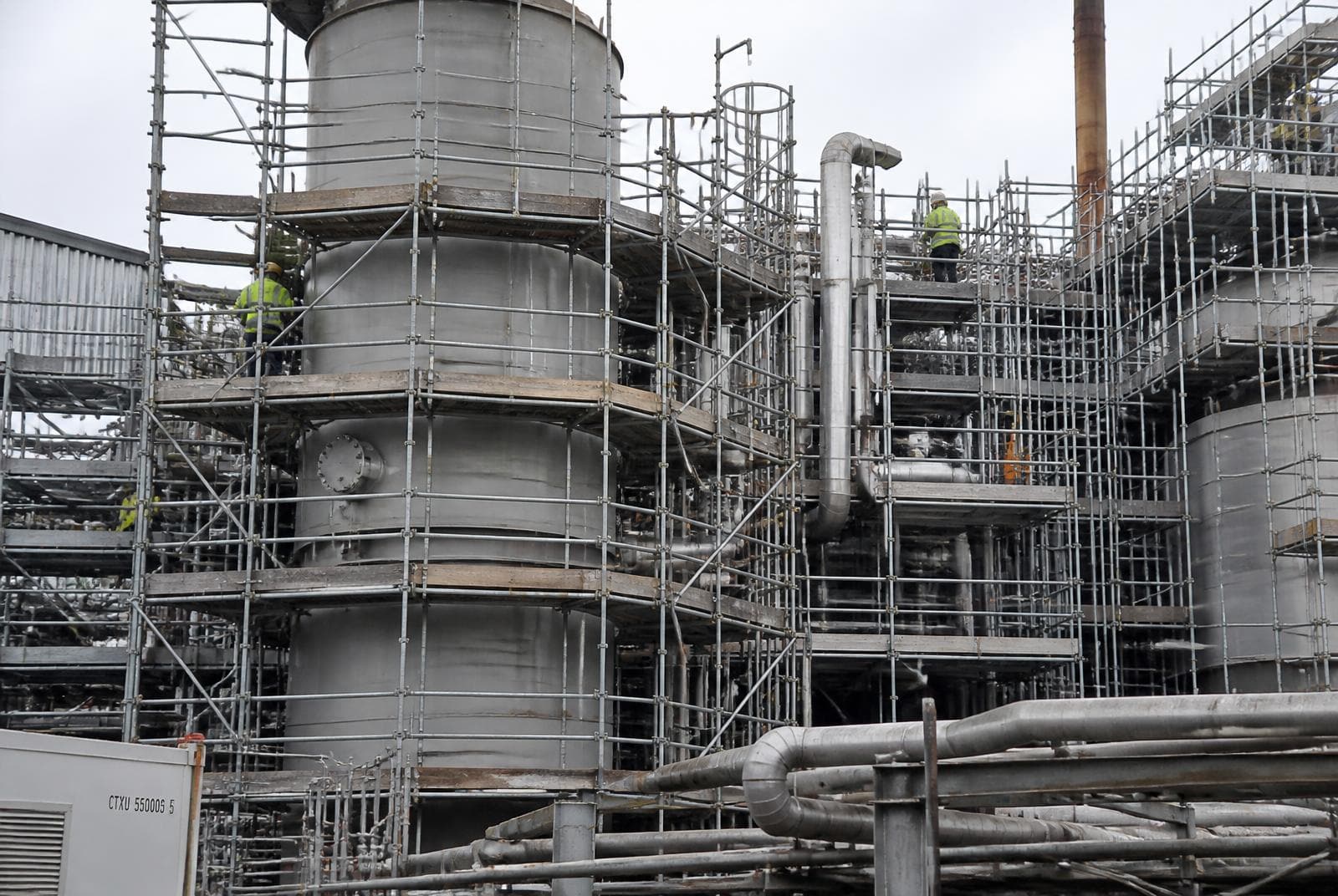 Heavy industrial system scaffolding built around steel silos and pipework at a UK industrial plant with scaffolders working at height.