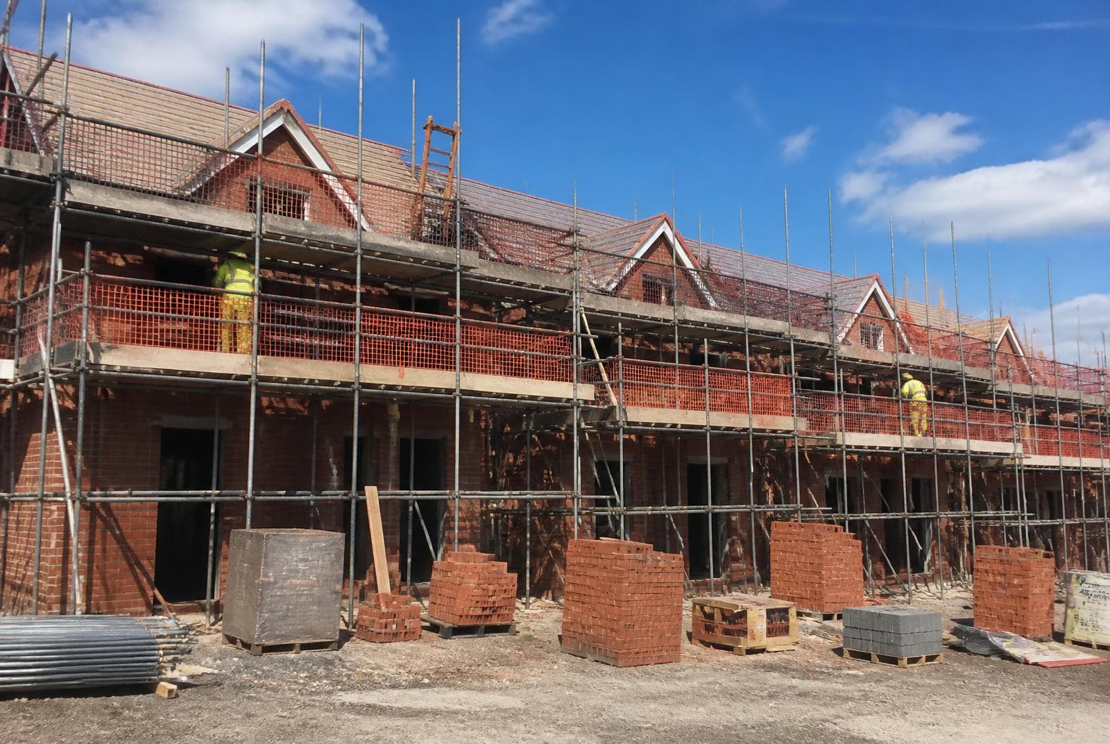 Neat uniform scaffolding with brick guards and netting across a row of new build houses on a UK housing development.