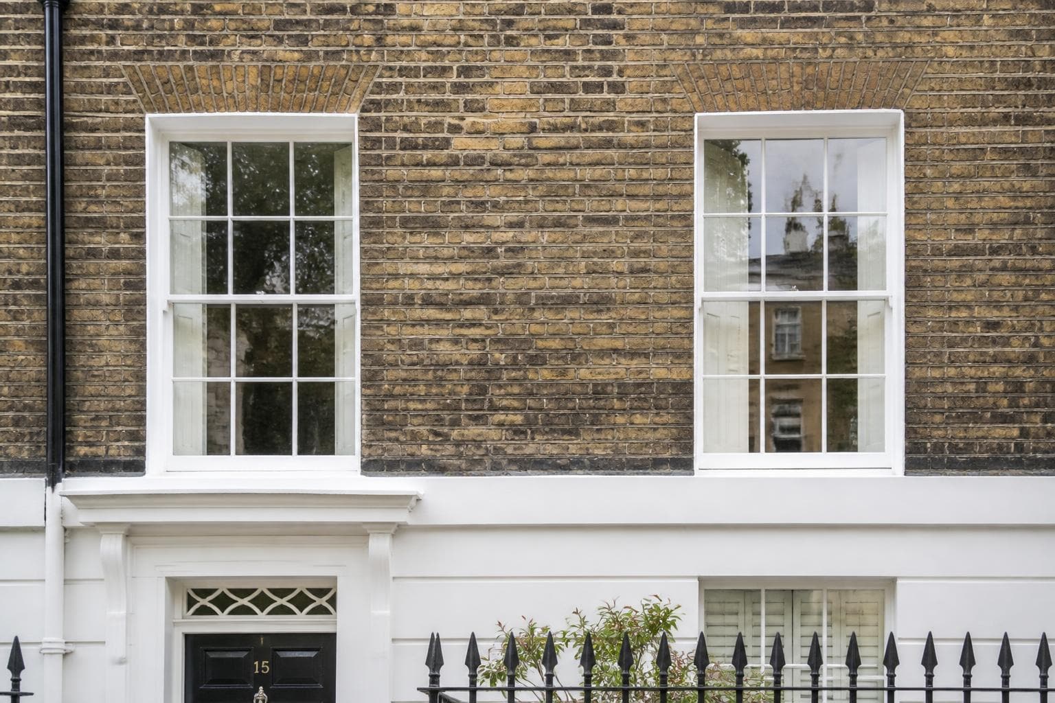 White heritage sliding sash windows on the brick facade of a Georgian UK townhouse.