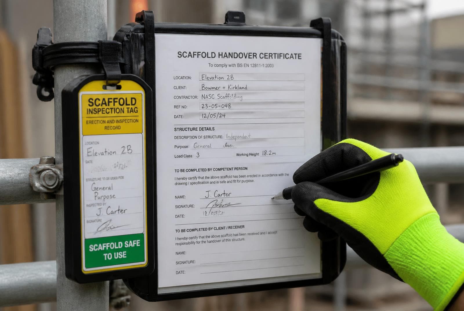 Gloved hand signing a scaffold handover certificate beside a green scaffold inspection tag fixed to a scaffold standard.