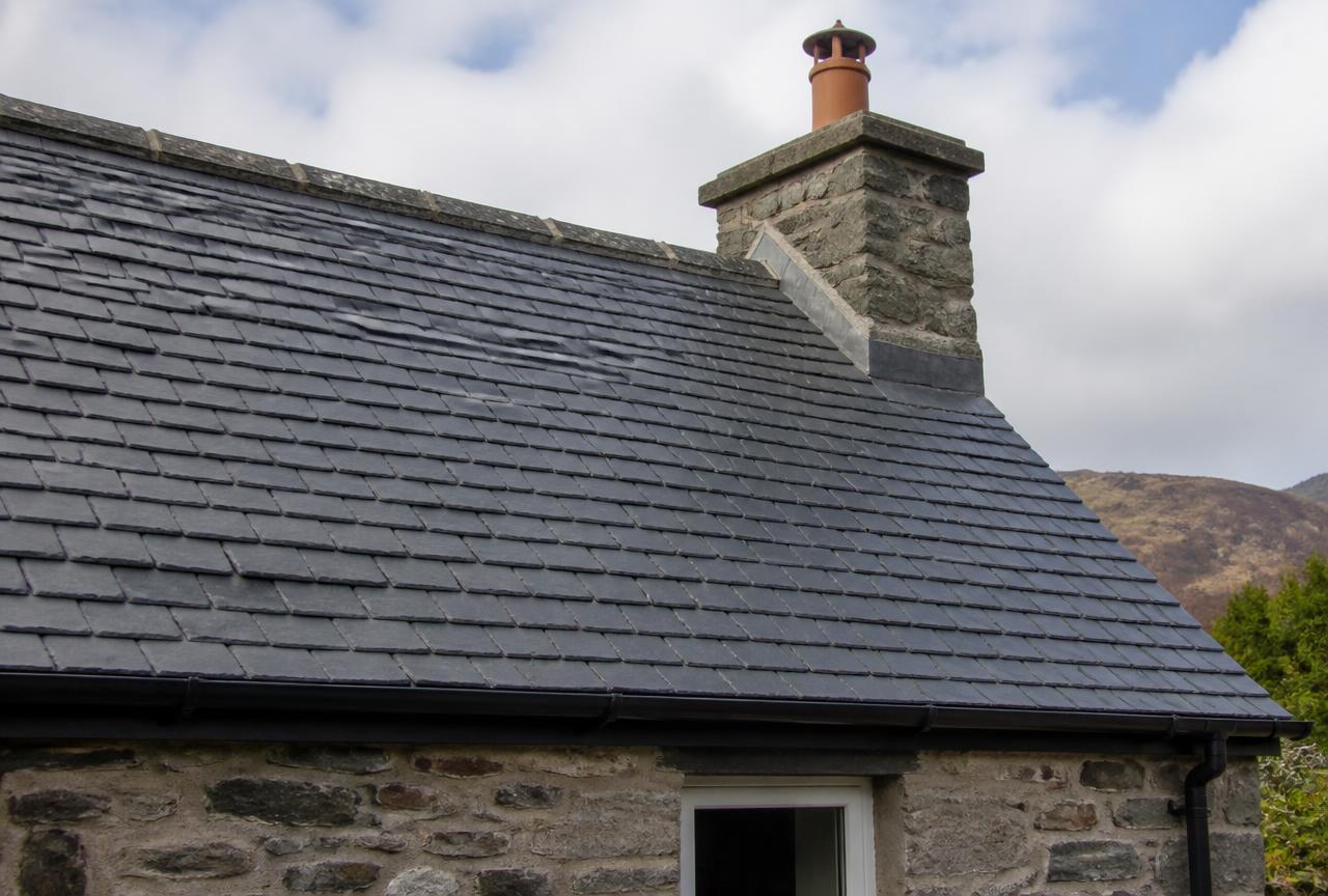 Traditional Welsh slate pitched roof on a UK stone cottage with new lead flashing around the chimney stack.