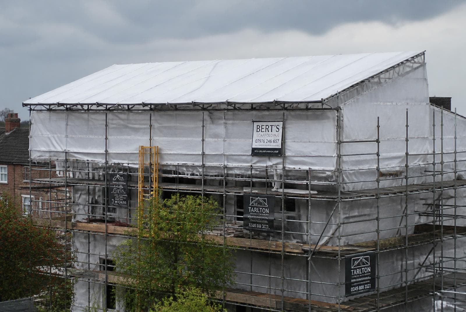 Temporary roof scaffold with white shrink wrap sheeting and aluminium beams covering a UK building undergoing a full re-roof.