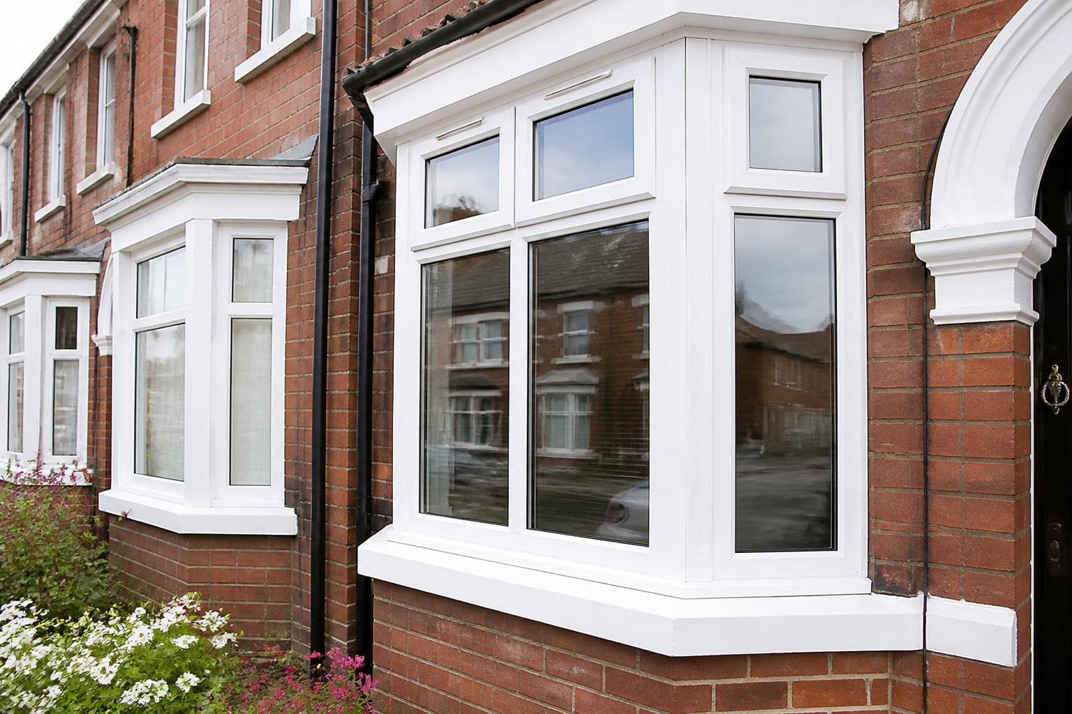 Newly installed white uPVC casement and bay windows across the front of a red brick UK terraced house.
